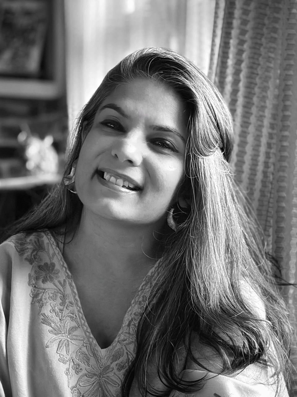 Bhavana smiling, seated by a window in soft daylight